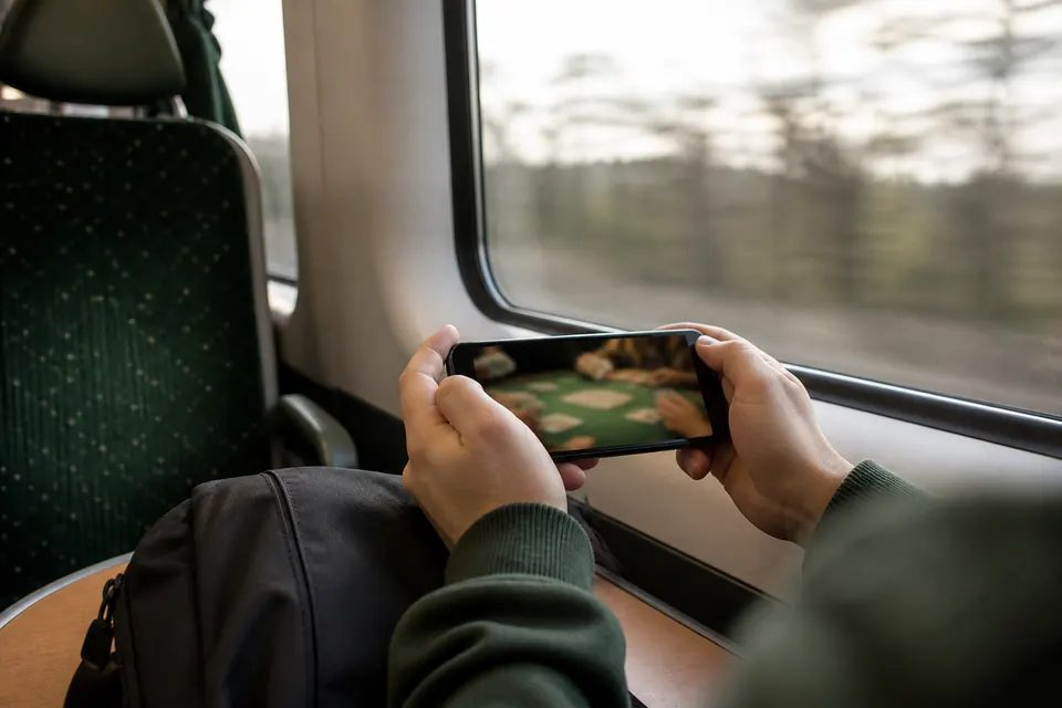 Händer håller en mobiltelefon i liggande läge med ett livebord på skärmen på ett tåg