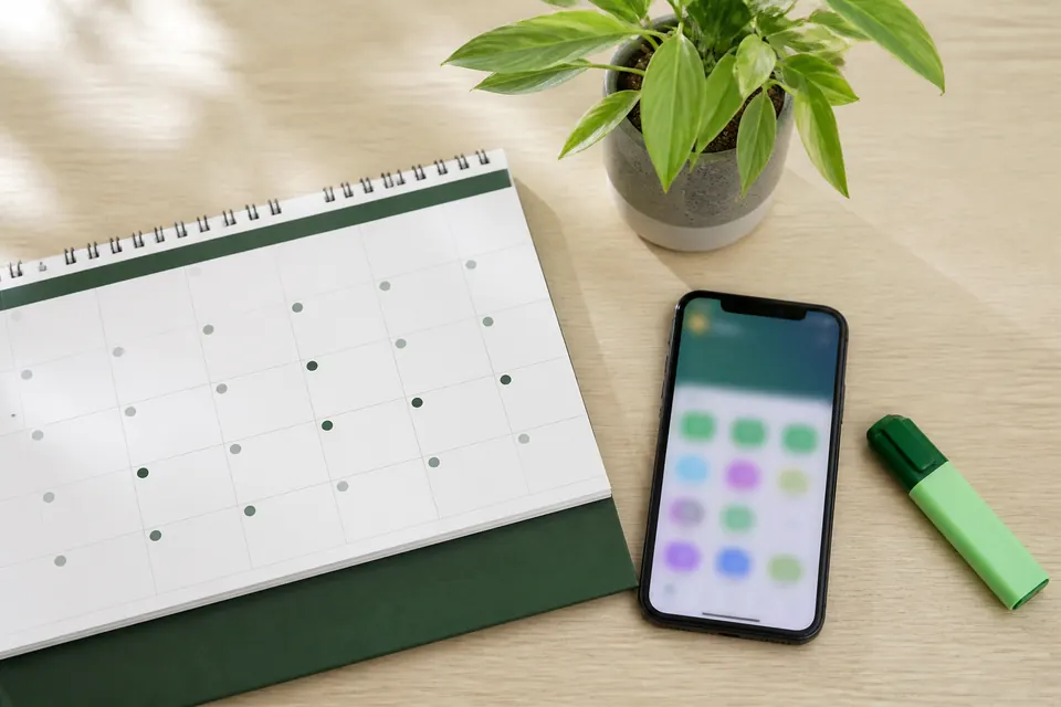 Bordskalender, mobiltelefon och överstrykningspenna på ett ljust skrivbord